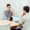 two students are engaged in a conversation in a study room with their laptops open in front of them.