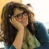 A bespectacled student, her face resting in her left hand, smiles during a class lecture.
