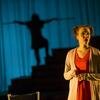 Women stands on stage with a shadow of a man behind her.