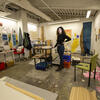 A student in black clothing paints in an art studio. 