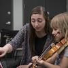 A Temple music student works with an elementary school student during a violin lesson.