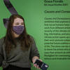 A masked Tyler student holds a phone as they stand in front of their work in a gallery.